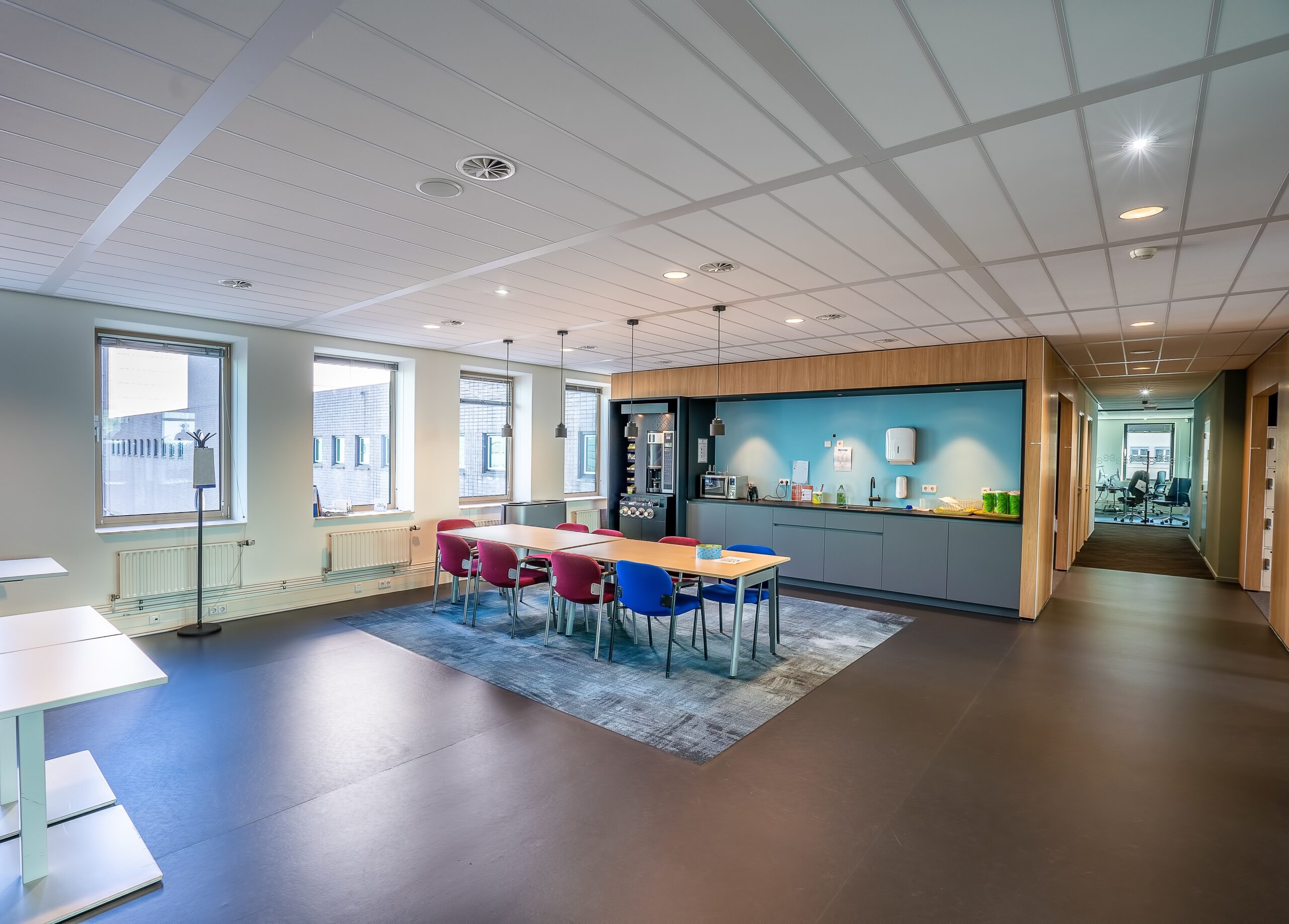 The interior of the kitchen area of a modern office with a long wooden table and chairs